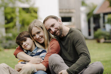 Happy family sitting on grass in their garden - KNSF07319