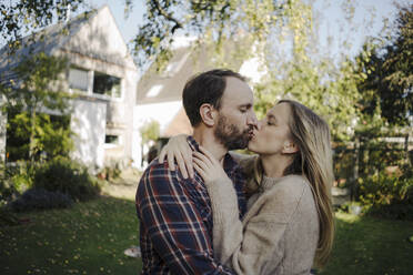 Happy couple kissing in garden, in front of their dream house - KNSF07334