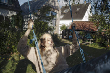 Blond woman swinging in her garden - KNSF07337