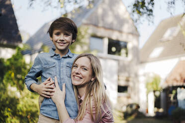 Mother embracing son in the garden of their home - KNSF07347