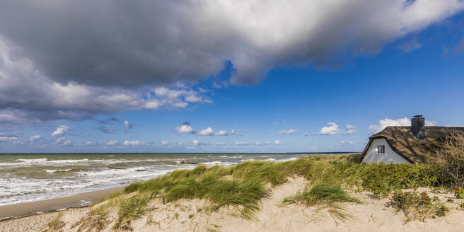 Deutschland, Mecklenburg-Vorpommern, Ahrenshoop, Wolken über Haus mit Reetdach am Sandstrand der Ostsee - WDF05664