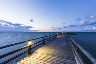 Deutschland, Mecklenburg-Vorpommern, Prerow, Beleuchtete Seebrücke in der Abenddämmerung mit klarer Horizontlinie über der Ostsee im Hintergrund - WDF05677