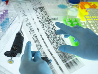 Hands of scientist wearing surgical gloves analyzing DNA sequencing result chart - ABRF00664