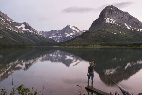 Rückansicht eines Wanderers mit Blick auf den Mt. Grinnell, während er auf dem Holz am Swiftcurrent Lake steht, lizenzfreies Stockfoto
