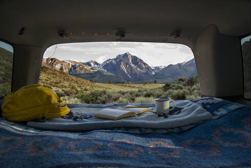 Tasche, Buch und Tasse auf einer Decke im Kofferraum eines Autos mit Mount Morrison im Hintergrund - CAVF73567