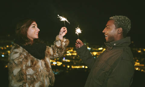 Glückliches junges Paar steht von Angesicht zu Angesicht und hält Wunderkerzen in der Nacht, lizenzfreies Stockfoto