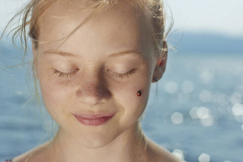 Close-up of woman with ladybug on her cheeks - CAVF73587