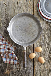 Overhead view of skillet pan with brown eggs and napkin on wooden table - CAVF73605
