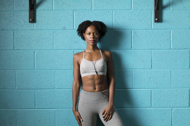Porträt einer selbstbewussten Frau, die Musik hört, während sie in einem Fitnessstudio an der Wand trainiert - CAVF73661
