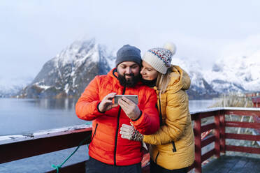 Touristenpaar mit Smartphone in Hamnoy, Lofoten, Norwegen - DGOF00083