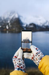 Nahaufnahme eines Touristen, der ein Smartphone-Foto in Hamnoy, Lofoten, Norwegen, aufnimmt - DGOF00100