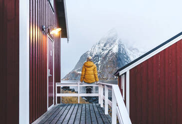 Tourist auf einer Veranda und genießt die Aussicht auf Hamnoy, Lofoten, Norwegen - DGOF00112