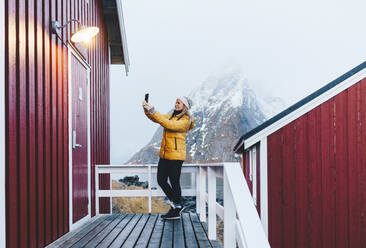 Tourist macht ein Selfie auf einer Veranda in Hamnoy, Lofoten, Norwegen - DGOF00113