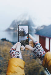 Nahaufnahme eines Touristen, der ein Smartphone-Foto in Hamnoy, Lofoten, Norwegen, aufnimmt - DGOF00114