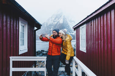 Touristenpaar macht ein Selfie auf einer Veranda in Hamnoy, Lofoten, Norwegen - DGOF00118