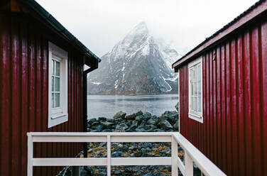 Rote Hütten und schneebedeckte Berge an der Küste, Hamnoy, Lofoten, Norwegen - DGOF00121