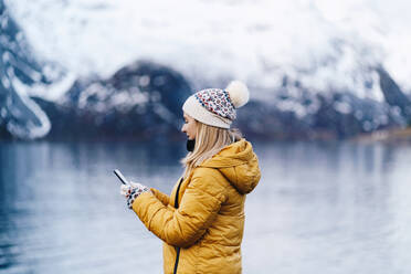 Tourist mit Smartphone in Hamnoy, Lofoten, Norwegen - DGOF00135