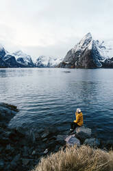 Tourist sitting on a rock enjoying the view at Hamnoy, Lofoten, Norway - DGOF00146