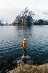 Tourist steht auf einem Felsen und genießt die Aussicht bei Hamnoy, Lofoten, Norwegen - DGOF00147
