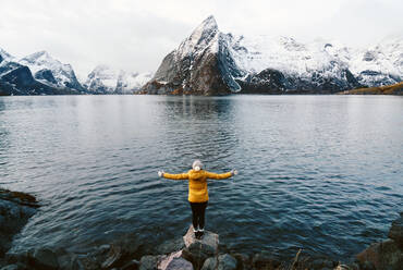 Tourist standing on a rock enjoying the view at Hamnoy, Lofoten, Norway - DGOF00149