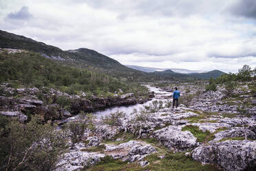 Mann steht über einem Flussufer mit Bergen, Lakselv, Norwegen - DHEF00077