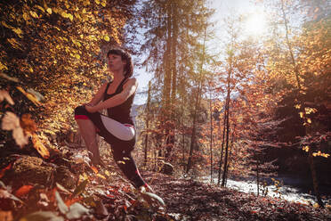 Woman jogging in autumn forest, stretching for warm up - DHEF00089