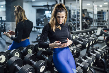 Frau macht eine Pause im Fitnessstudio und benutzt ihr Smartphone - OCMF00996