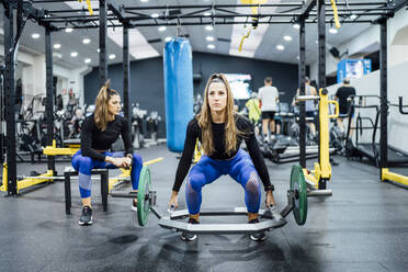 Frau trainiert im Fitnessstudio mit Zwillingsschwester, die eine Pause macht - OCMF00998