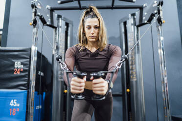 Frau trainiert an einer Kabelmaschine im Fitnessstudio - OCMF01006