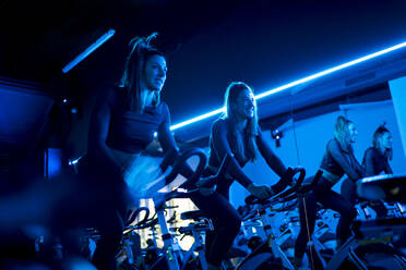 Smiling twin sisters exercising on spinning bikes in gym - OCMF01008