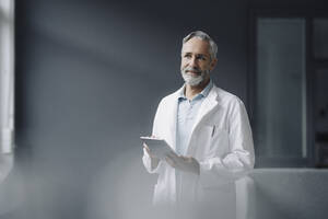 Porträt eines Arztes mit digitalem Tablet, der in die Ferne schaut - KNSF07354
