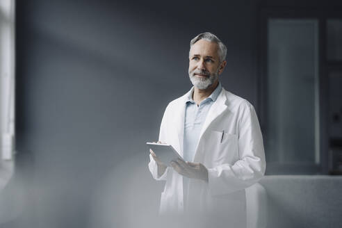Portrait of doctor with digital tablet looking at distance - KNSF07354