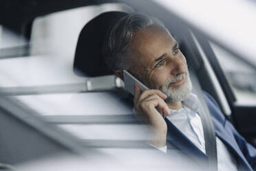 Porträt eines lächelnden reifen Geschäftsmannes, der in seinem Auto telefoniert - KNSF07372