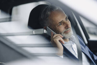 Portrait of smiling mature businessman on the phone in his car - KNSF07372