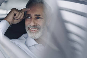 Portrait of smiling mature businessman in his car looking at distance - KNSF07375