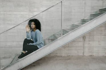 Schöne junge Frau sitzt auf einer Treppe hinter einer Glasscheibe - TCEF00098