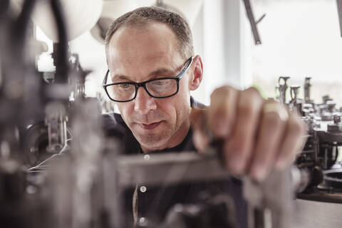 Porträt eines konzentrierten Mannes bei der Arbeit an einer Maschine in einer Textilfabrik, lizenzfreies Stockfoto