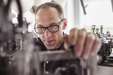 Porträt eines konzentrierten Mannes bei der Arbeit an einer Maschine in einer Textilfabrik - SDAHF00058