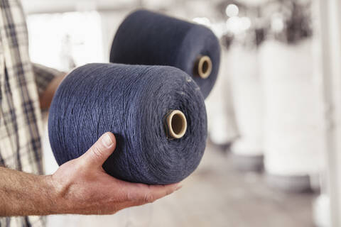 Nahaufnahme eines Mannes, der Baumwollspulen in einer Textilfabrik hält, lizenzfreies Stockfoto