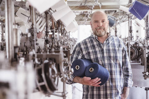 Porträt eines Mannes mit Baumwollspulen in einer Textilfabrik, lizenzfreies Stockfoto