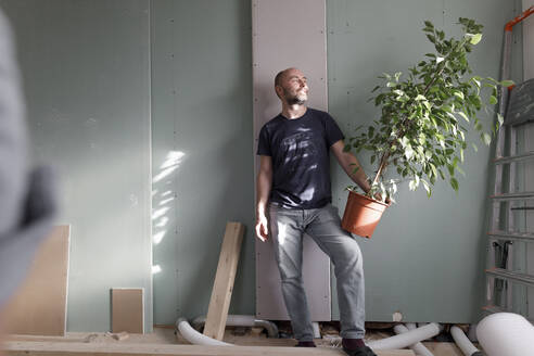 Mann hält Zimmerpflanze auf Baustelle zu Hause - KMKF01224