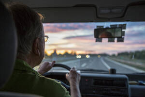 Älterer Mann am Steuer eines Autos auf einer Autobahn bei Sonnenuntergang - MAMF01063