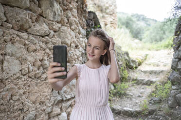 Mädchen macht Selfie neben einer alten Steinmauer, Frankreich - BFRF02193