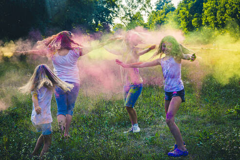 Gruppe von zwei Frauen und zwei Mädchen, die das Fest der Farben auf einer Wiese feiern - SARF04454