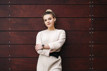 Portrait of a young woman standing at a wooden wall - DGOF00184