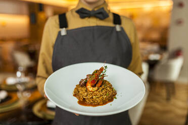 Kellnerin serviert Paella auf weißem Teller - VABF02572