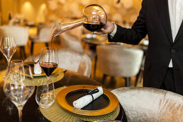 Kellner gießt in einem schicken Restaurant Wein aus einer Karaffe in ein Glas - VABF02575