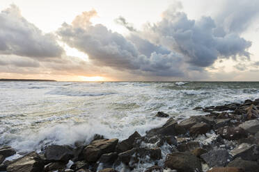 Deutschland, Mecklenburg-Vorpommern, Warnemünde, Meereswellen brechen gegen Felsen bei Sonnenuntergang - WDF05717