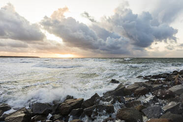 Germany, Mecklenburg-West Pomerania, Warnemunde, Sea waves crashing against rocks at sunset - WDF05717