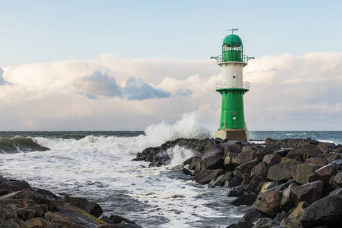 Deutschland, Mecklenburg-Vorpommern, Warnemünde, Leuchtturm und Meereswellen, die gegen Felsen schlagen - WDF05720